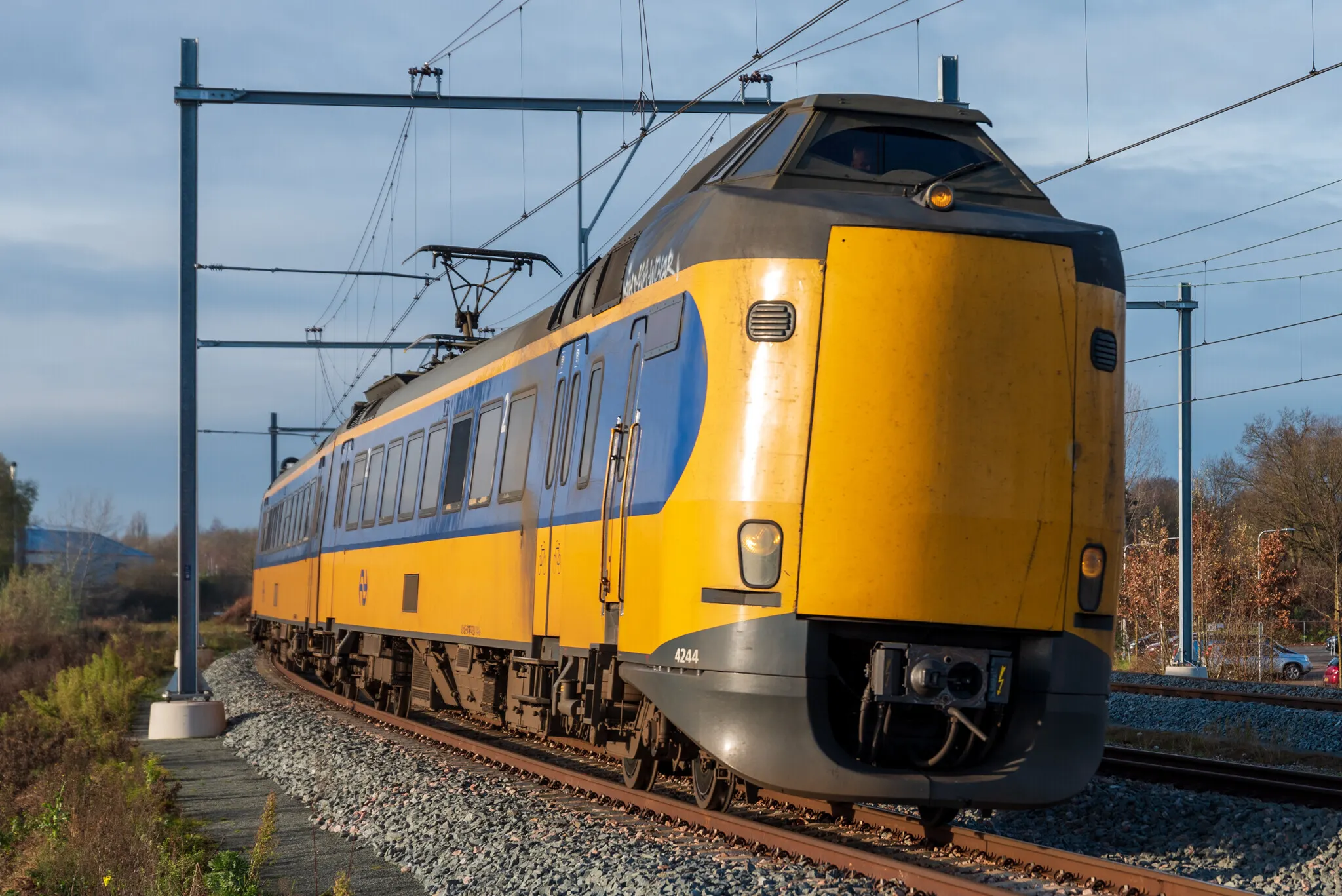treinen - ZwolleInside Yellow and blue electric passenger train on a curved track with overhead power lines nearby.